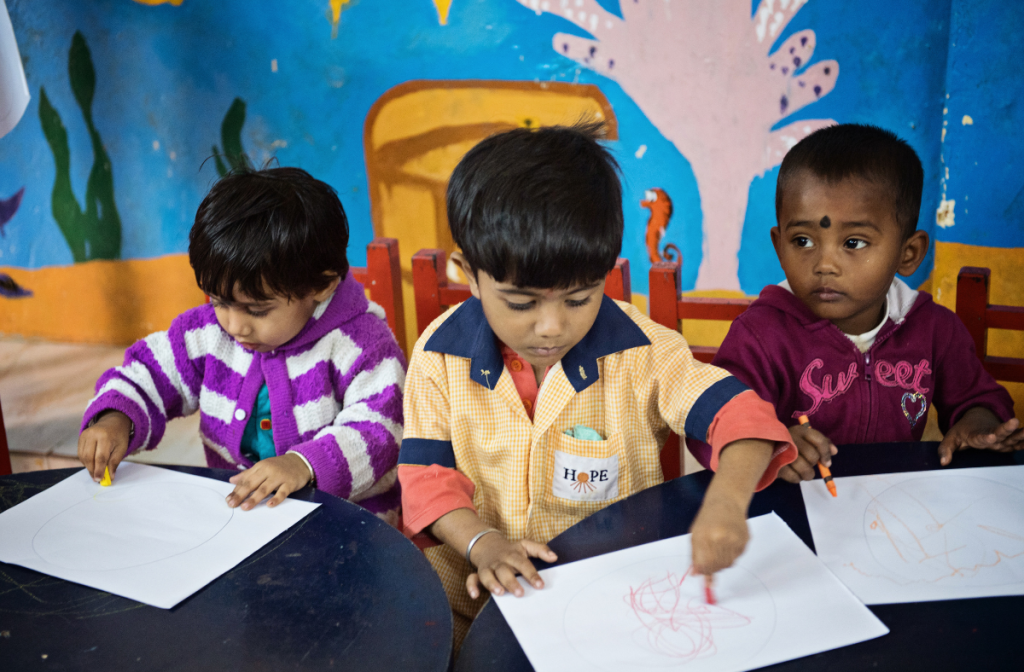 Three little children at the creche drawing pictures.