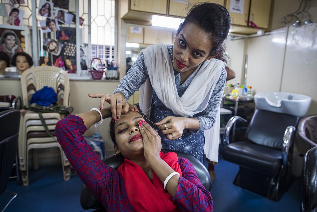 A trainee beautician threads the eyebrows of a young woman
