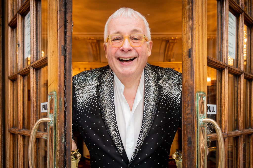 Christopher Biggins stands between open doors and smiles
